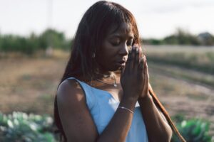 Afro Girl closed her eyes, praying in a outdoors. Hands folded in prayer concept for faith